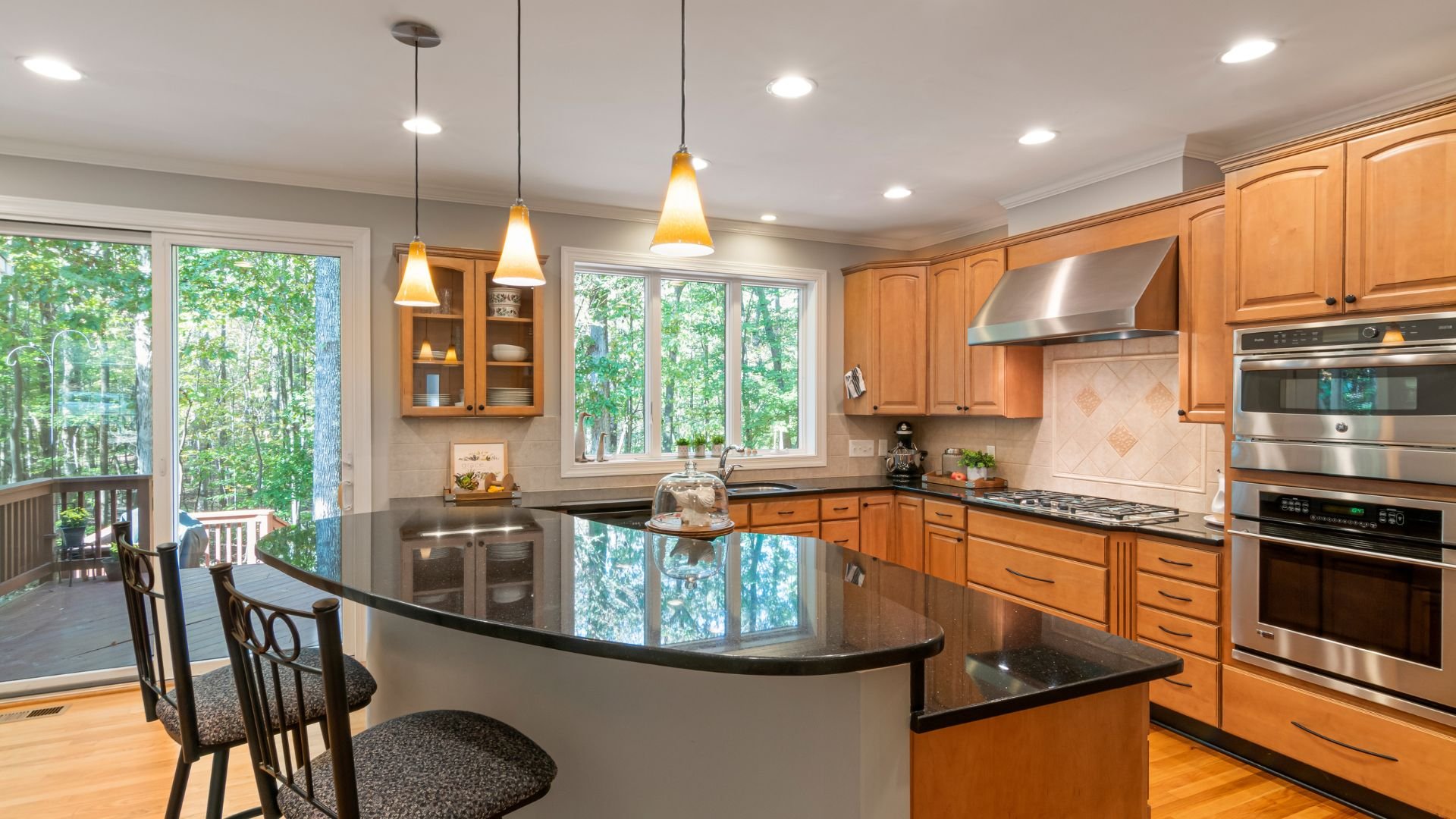 Modern kitchen with wood cabinets, black countertop, and forest view